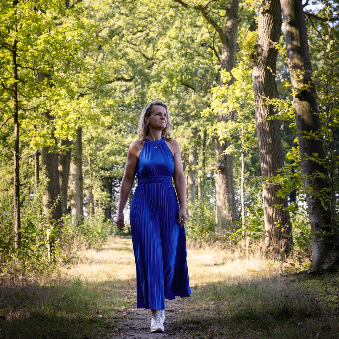 Esther loopt in een lange blauwe jurk over een bospad